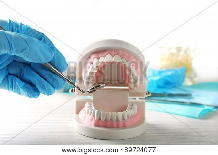 White fake teeth in hand of dentist, on light background
