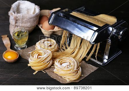 Metal pasta maker machine and ingredients for pasta on wooden background
