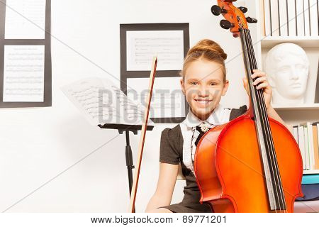 Smiling girl holds string to play violoncello