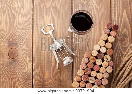 Wine bottle shaped corks, glass of wine and corkscrew over rustic wooden table background. View from above with copy space