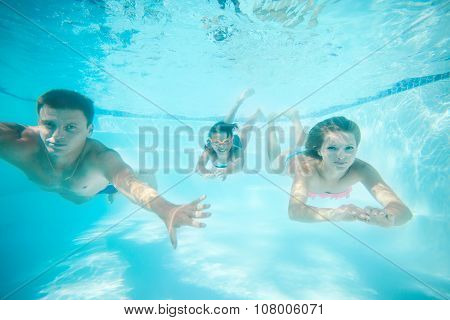 Parents and daughter swimming underwater in pool.