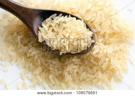 Small Heap Of Parboiled Rice With A Wooden Spoon On White, Closeup Shot