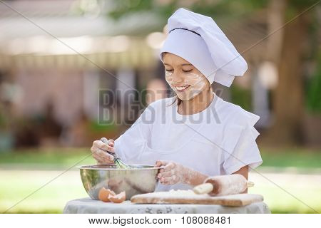 Happy little chef whipping eggs in a bowl outdoors