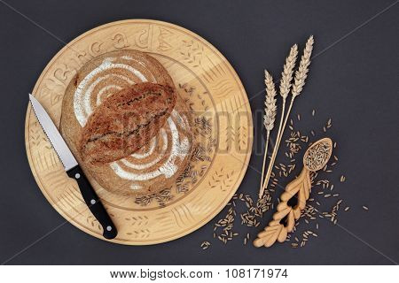 Homemade rye bread loaf on a wooden board with knife, grain and wheat sheaths with carved lovespoon on grey background.