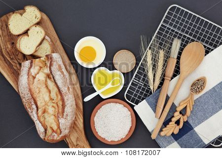 French bread loaf with baking ingredients and utensils with wheat sheaths and grain in a lovespoon on grey  background.