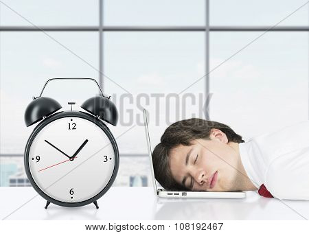 Relaxing Professional On The Laptop In The Panoramic Office. An Alarm Clock Is On Foreground.