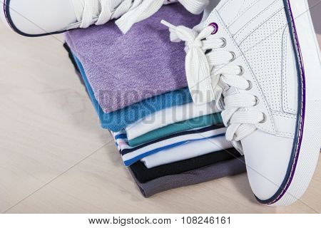 Fashion Ideas And Concepts. Pair Of White Fasionable Sneakers Close To Stack Of Prepared Clothing.