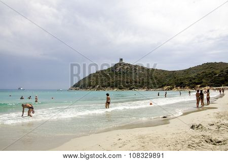 Porto Giunco, Italy-august 23: Unidentified People In Blue Beach With Some People And Grey Cloudy Sk