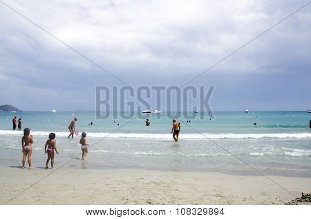 Porto Giunco, Italy-august 23: Unidentified People In Blue Beach With Some People And Grey Cloudy Sk