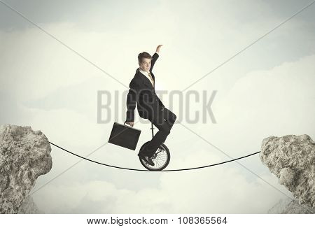 Brave business man riding an mono cycle between cliffs concept