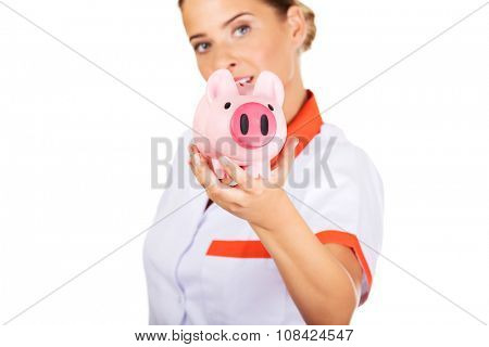 Young beautiful female doctor or nurse holding a piggybank.