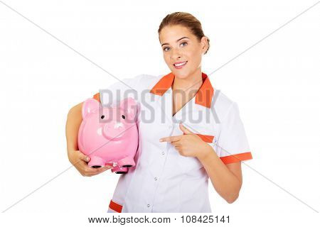 Young beautiful female doctor or nurse holding a piggybank.