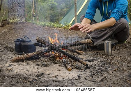 Girl Sitting While Camping Near The Fire Heated And Drink Hot Tea