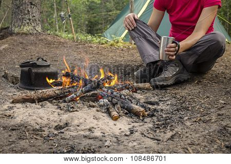 Girl Sitting While Camping Near The Fire Heated And Drink Hot Tea