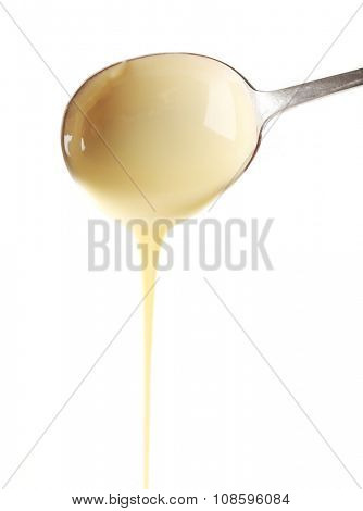 Condensed milk pouring from a spoon, isolated on white