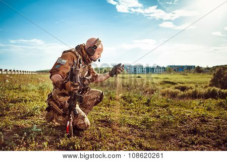 Military Pathfinder Is Looking At The Soil In His Hand. Ruined City On The Background.