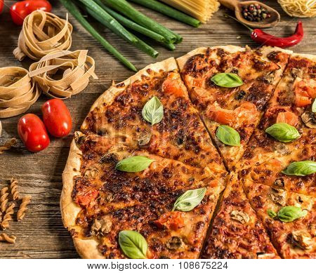 Italian food background with pizza, raw pasta and vegetables on wooden table