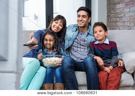 Happy young family eating popcorn while watching tv in living room