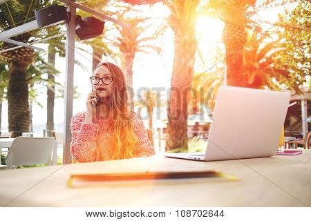beautiful female designer talking on her smart phone while sitting front open laptop computer