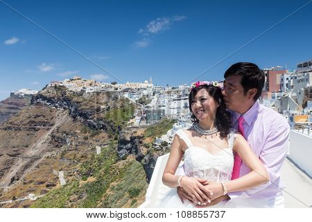 A Couple Of Newlywed’s Tourists Pose On A Balcony With The View Of Santorini Island, In Greece. Tour