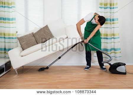Man Lifting Couch While Cleaning Floor With Vacuum Cleaner