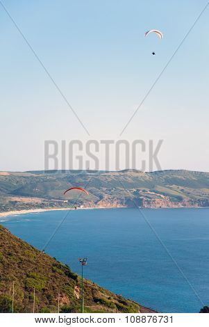 Two Parachute Flying In Sardinian Coast With Sea And Mountain Behind