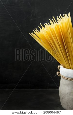 Uncooked Spaghetti in Earthen Jar on Black Background. Menu Poster Template Copy Space Text Ready. Mediterranean Healthy Diet.