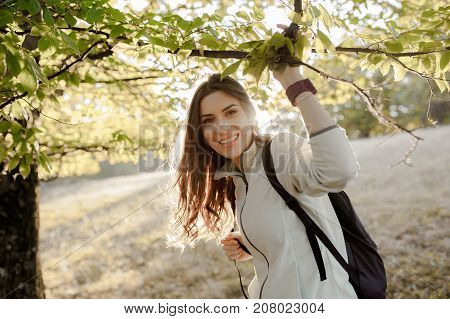 Young woman casual dressed, with backpack in the forest on afternoon light in the autumn season, going for a walk, enjoying tine in nature..
