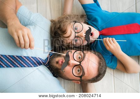 Funny man and kid with fake mustache. Happy family playing in home