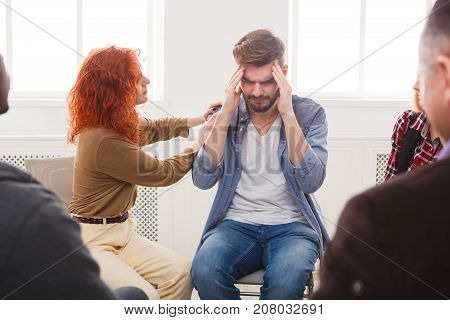 Meeting of support group. Young depressed man with headache sitting at rehab group therapy. Psychotherapy, depression, life issues concept