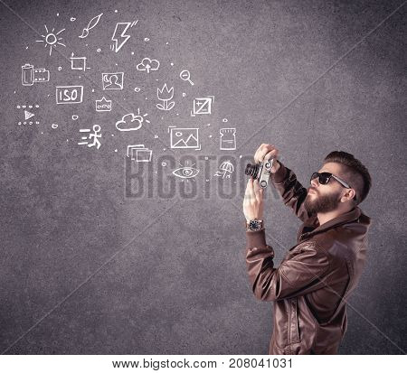 An elegant hipster guy trying to use a vintage camera with camera settings icons drawn on wall, like flash, white balace or ISO value concept