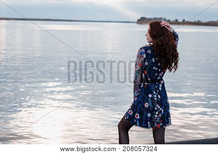 Young beautiful brunette woman in blue dress on the autumn river embankment.