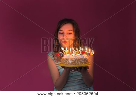 Young woman blowing out candles on a birthday cake over gray background
