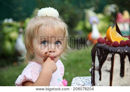 Girl birthday. A little white-haired girl of two years is trying a birthday cake. Little girl celebrating second birthday.
