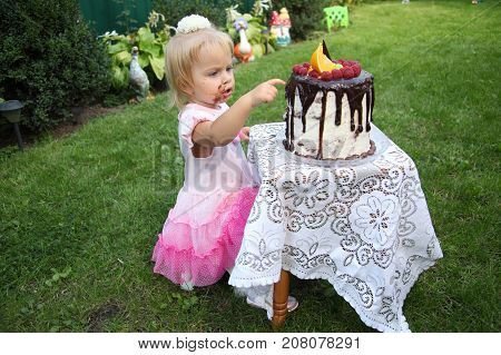 Girl birthday. A little white-haired girl of two years is trying a birthday cake. Little girl celebrating second birthday.