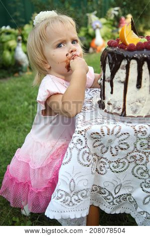 Girl birthday. A little white-haired girl of two years is trying a birthday cake. Little girl celebrating second birthday.
