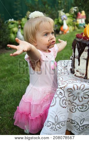 Girl birthday. A little white-haired girl of two years is trying a birthday cake. Little girl celebrating second birthday.