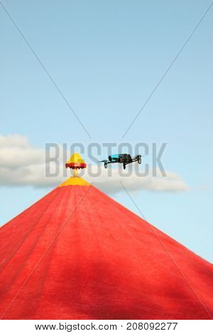 Blue drone flying over red circus tent against a blue sky and white clouds in summer time and shoots a video