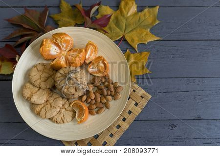 Tasty almond cookies on a wooden plate surrounded by autumn leaves