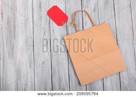 A brown paper bag and an empty red tag on a gray wooden background. Close-up. The species is in full view. The concept is Christmas.