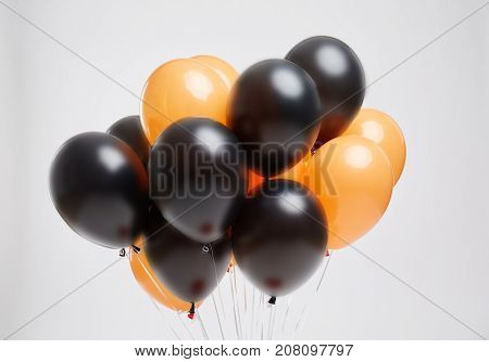 Close-up picture of bunch of orange and black flying air balloons for Halloween or birthday party on a light gray background.