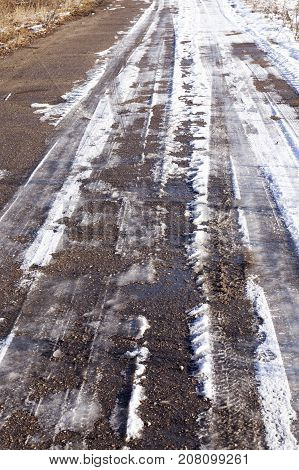 an old asphalt road covered with snow. Winter time of the year, ice lines are visible on the surface. Close-up photo