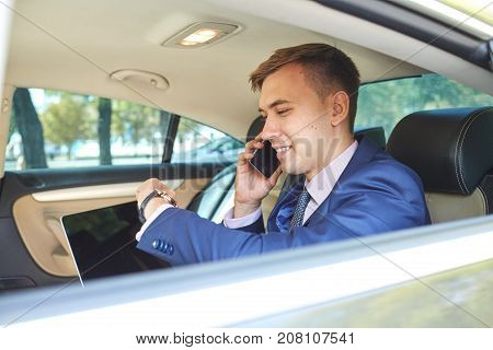 a young man sitting in the backseat of a car, looking at the clock, how much time talking on the phone and waits for the driver