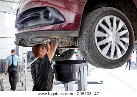 The mechanic works at the bottom of the car, which stands on the lift