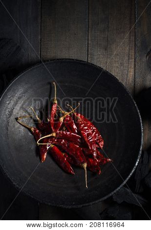 Dried red hot Indian chilies in a dark metal wok on wooden background. A rustic food photography background. View from above.