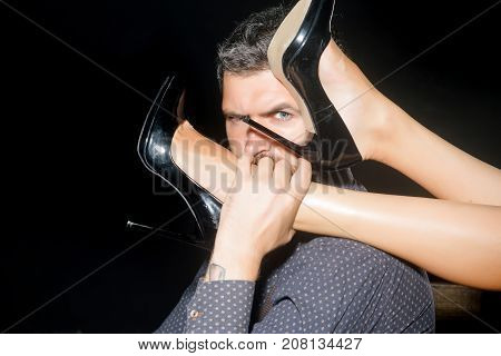 Romance and couple in love. Legs of woman in shoes at man with beard. Guy at table with female legs. Love and relations dominating. Man in shirt isolated on black background.