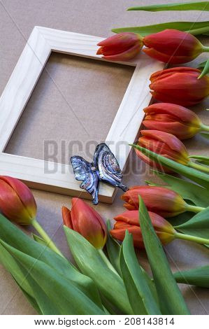 Glass blue butterfly on the wooden frame with many red tulips around