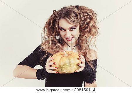 Portrait of woman holding in hands orange pumpkin isolated on gray background. Wearing black blouse and red skirt. Halloween celebration. Looking to camera and smiling