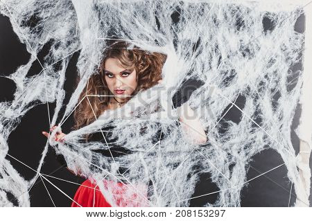 Halloween witch girl cought in spider network in a blouse and red skirt. Halloween concept. Vertical close-up shot