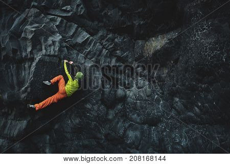 male rock climber. rock climber climbs on a black rocky wall on the ocean bank in Iceland, Kirkjufjara beach. man makes hard move without rope.
